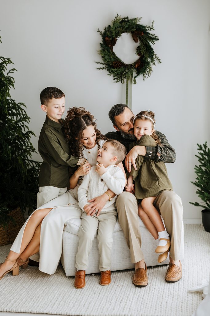 Family cuddling on neutral seating during a Christmas mini session in Louisville, KY