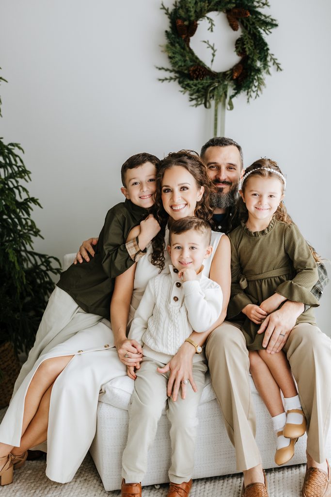 Family cuddling on neutral seating during a Christmas mini session in Louisville, KY